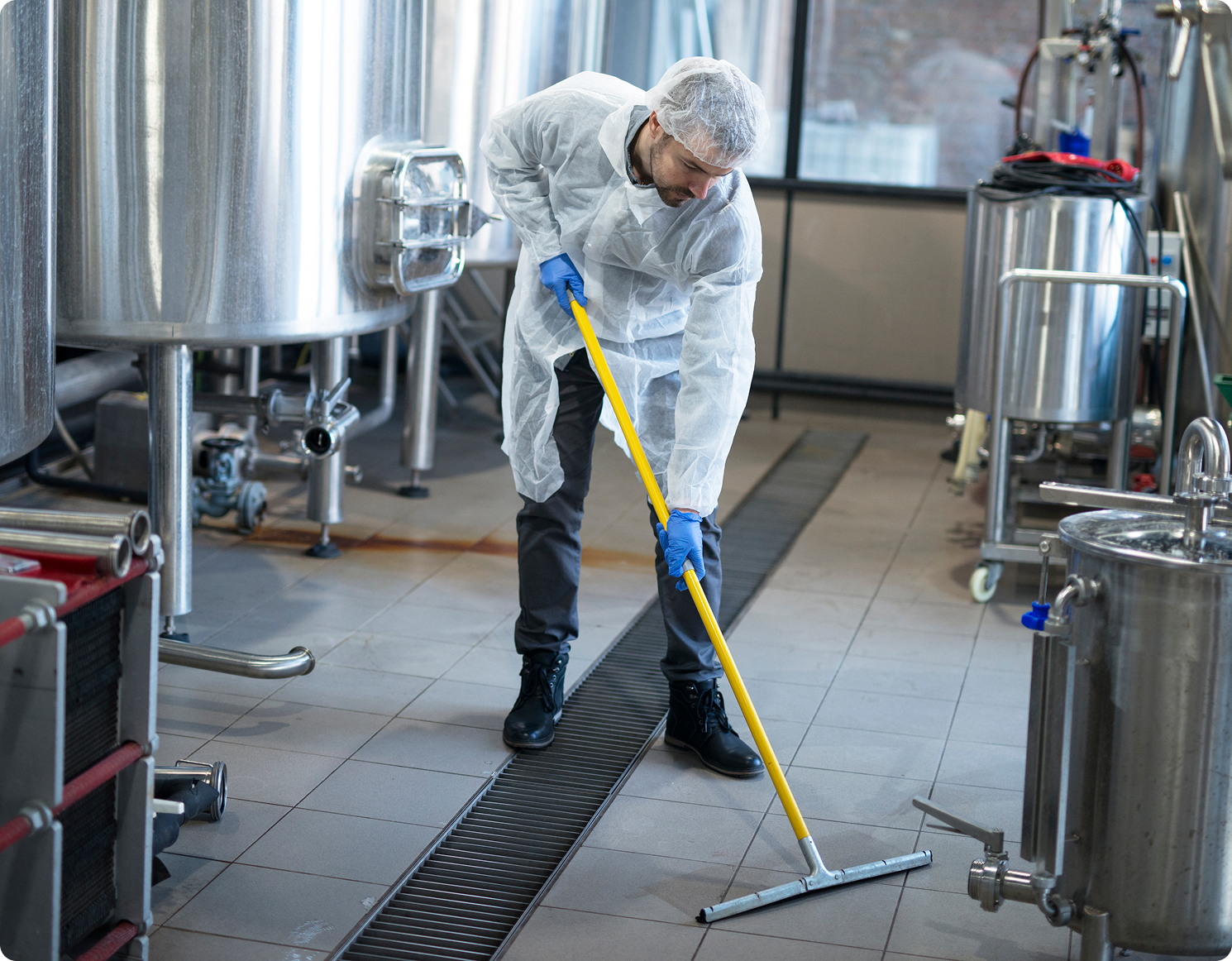 Worker cleaning industrial facility with squeegee.